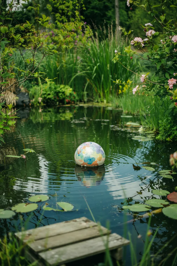 Ein malerischer Wasserbereich mit sanften Wellen, umgeben von üppigem Grün und bunten Blumen, ideal für Entspannung und Naturbeobachtungen. Der kleine Teich lädt zur Ruhe ein.