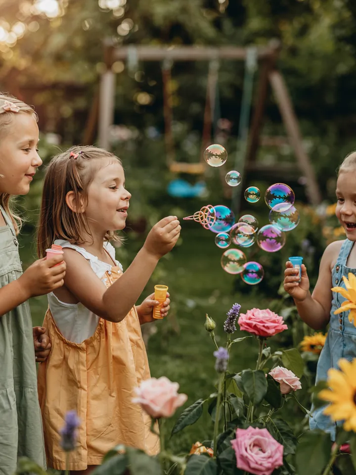 Ein fröhliches Kind im Freien, das mit einem Seifenblasenstab farbenfrohe Blasen erzeugt, ideal für kreative Aktivitäten im Kindergarten.