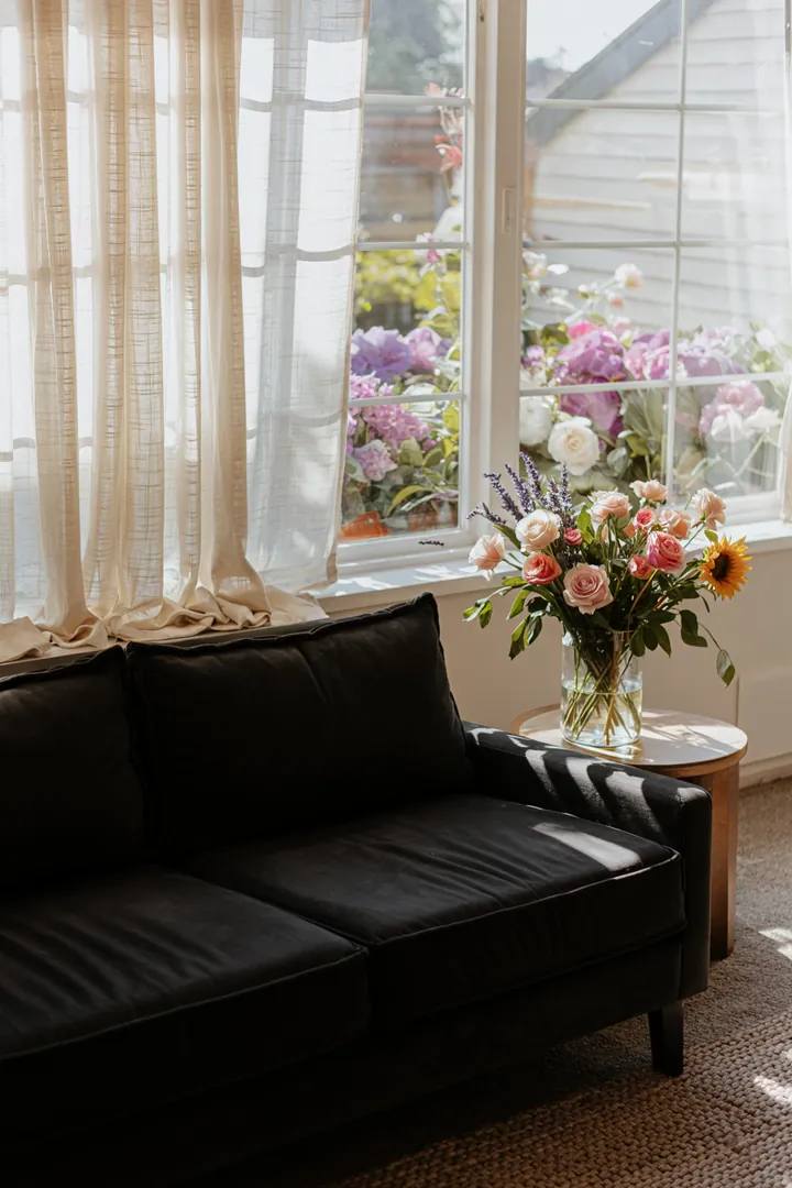 Ein stilvolles Wohnzimmer mit eleganten Stoffen, in dem ein modernes schwarzes Sofa harmonisch mit dekorativen Fenstern kombiniert wird.