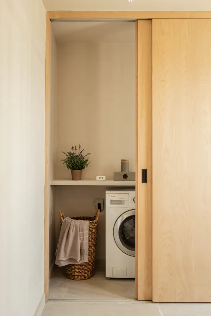 Ein heller Raum mit praktischen Lösungen zur Wäscheorganisation, der durch eine elegante Schiebetür zugänglich ist und eine stilvolle Waschküche versteckt.