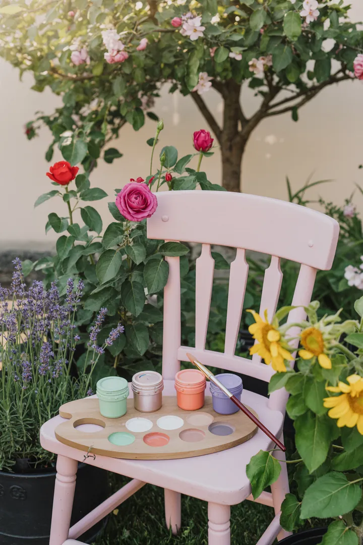 Ein Handwerker, der mit Pinsel und Farbe eine Outdoor-Sitzgarnitur aus Holz bearbeitet, um sie zu renovieren und zu schützen.