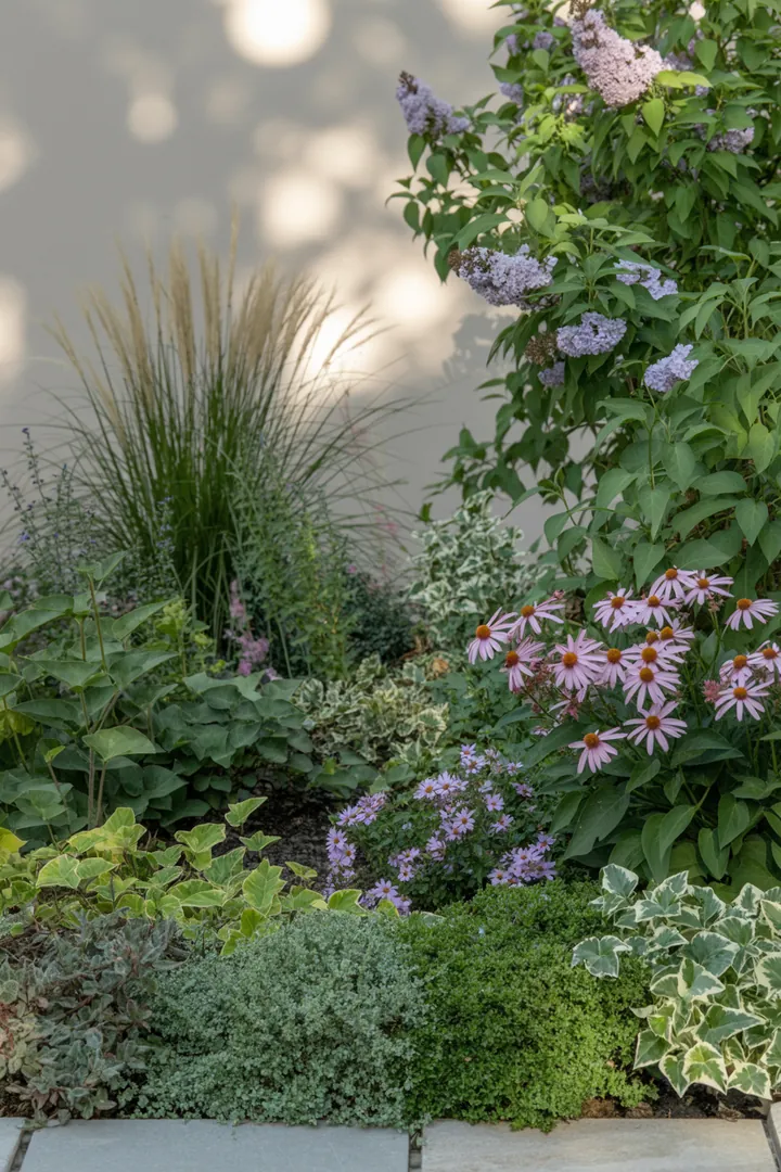 Eine stilvolle Gartenlandschaft mit dekorativen Randsteinen, die Beeteinfassungen umsetzen, umgeben von üppigen Gräsern, bunten Stauden und einem eleganten Pflanzkübel, der das Gesamtbild ergänzt und Unkrautvlies schützt.